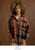 Model on brown textured background wearing plaid top.