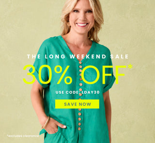 A smiling blonde woman wearing a teal short-sleeve button-front top stands against a textured light green background with large promotional text reading 'THE LONG WEEKEND SALE 30% OFF* USE CODE: LDAY30 SAVE NOW'.