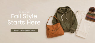 A styled flat-lay of fall fashion items on a light beige background, including an olive green hoodie, a brown suede shoulder bag, white pants, and a multicolor knit beanie. Large text on the left reads 'TRENDING Fall Style Starts Here' with a 'SHOP THE COLLECTION' button below.
