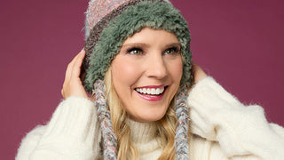 Model wearing winter knit hat on pink background.