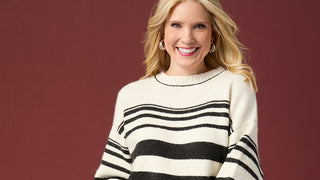 A smiling blonde woman wearing a cream knit sweater with bold black horizontal stripes, set against a solid dark reddish-brown background.
