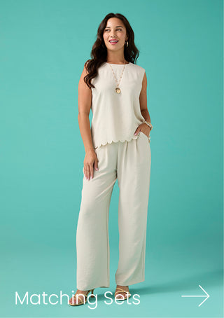 Woman wearing a white sleeveless top and pants against a teal background
