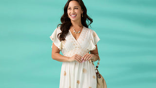 Woman in a white dress with gold patterns against a teal background