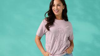 Woman wearing a pink floral embroidered top against a teal background