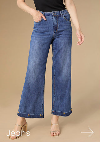 Model wearing dark denim wide leg jeans on tan background.